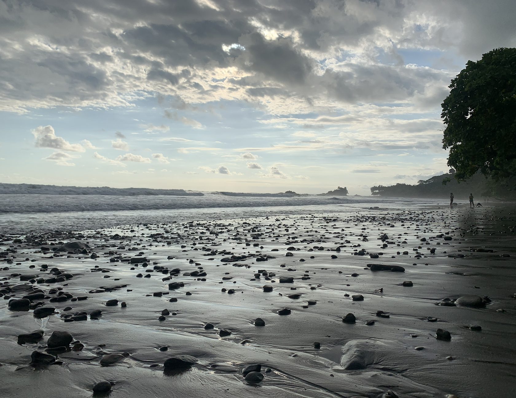 Playa de arena negra al atardecer con nubes dramáticas y oleaje fuerte en el Pacífico de Costa Rica