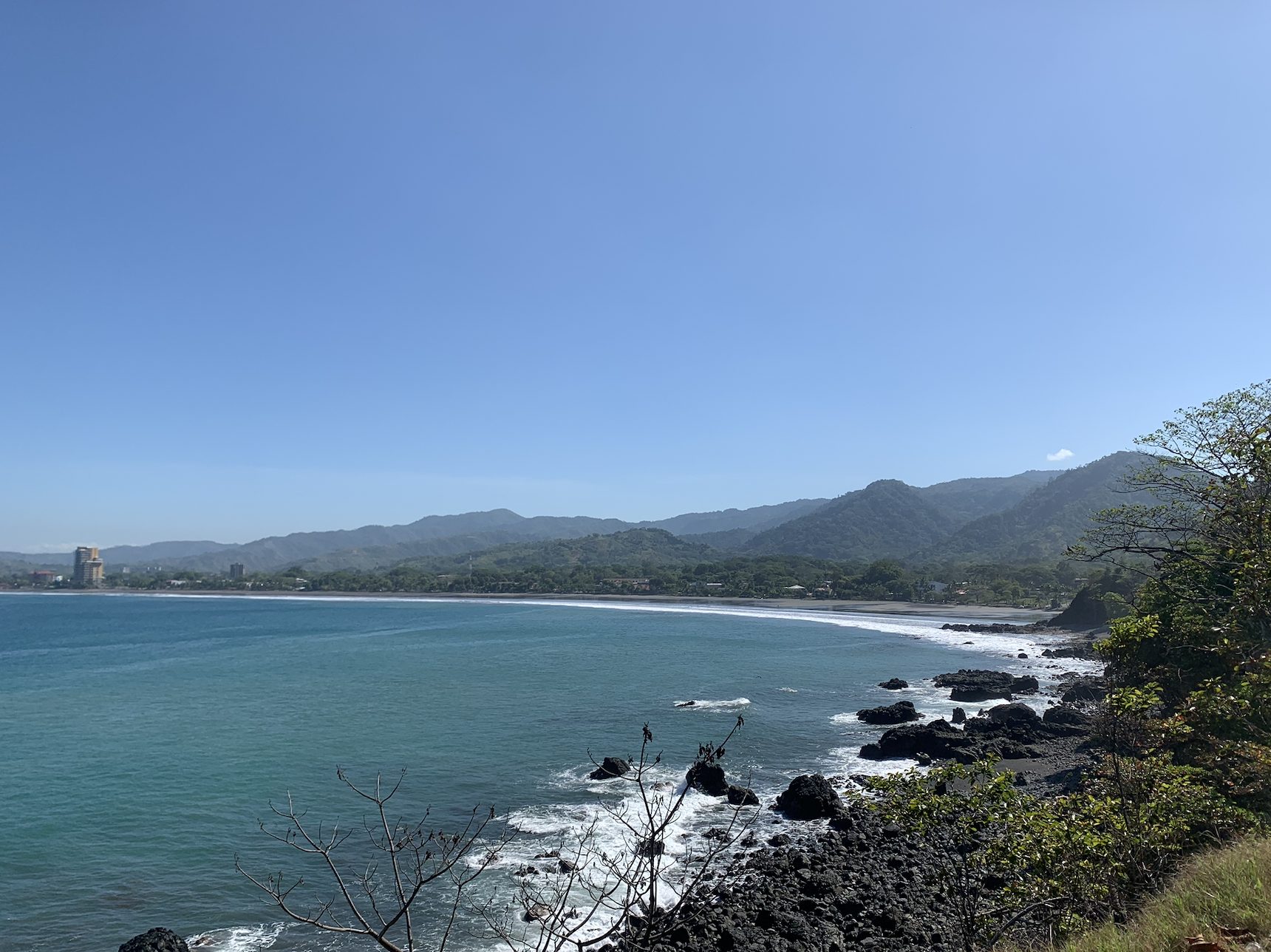 Vista de la costa Pacífica de Costa Rica desde un mirador, con playa de arena oscura y montañas de fondo