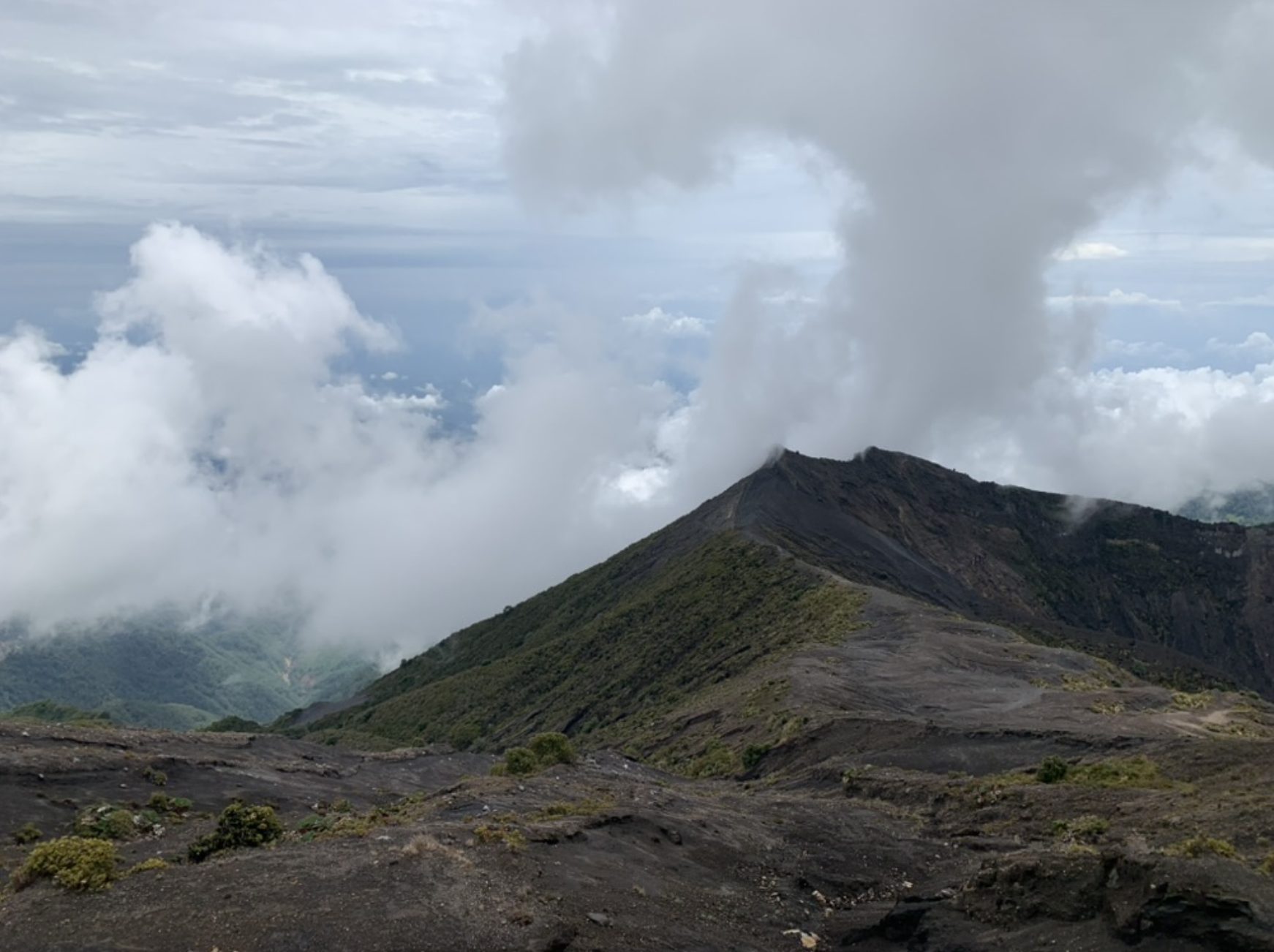 Cráter de un volcán activo en Costa Rica, con vapor volcánico elevándose entre las nubes