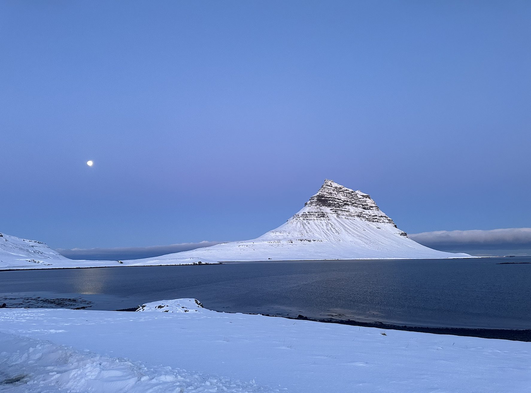 Montaña Kirkjufell al atardecer con la luna sobre el fiordo, Islandia